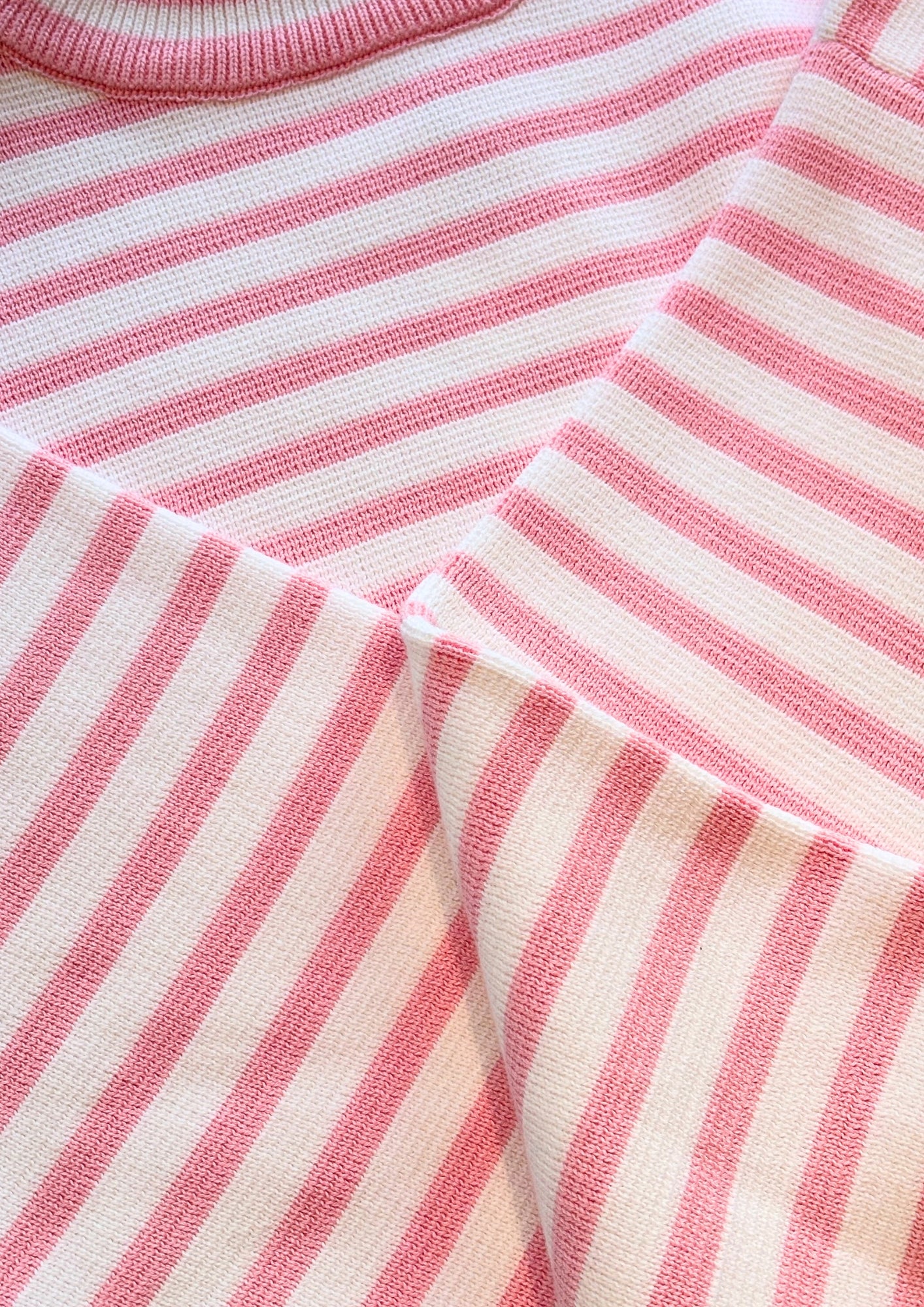Nahaufnahme des weichen Strickstoffs des Pullovers Sailor Rosa White, ordentlich gefaltet, um die horizontalen rosa und weißen Streifen zu zeigen.