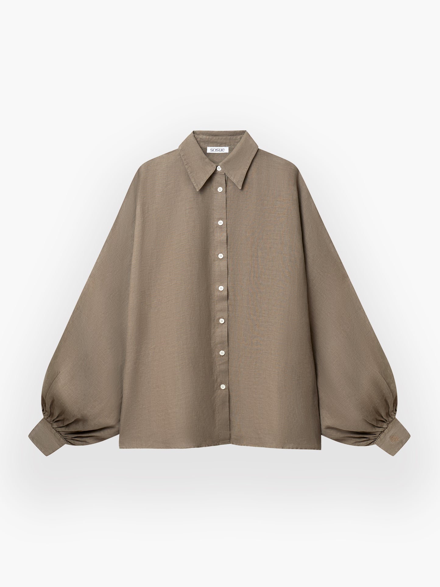 Das Antonia Linen Soft Brown ist ein locker sitzendes, langärmeliges taupefarbenes Hemd aus weichem Leinen mit spitzem Kragen, weißen Knöpfen auf der Vorderseite und weiten, an den Manschetten gerafften Ballonärmeln auf weißem Grund.