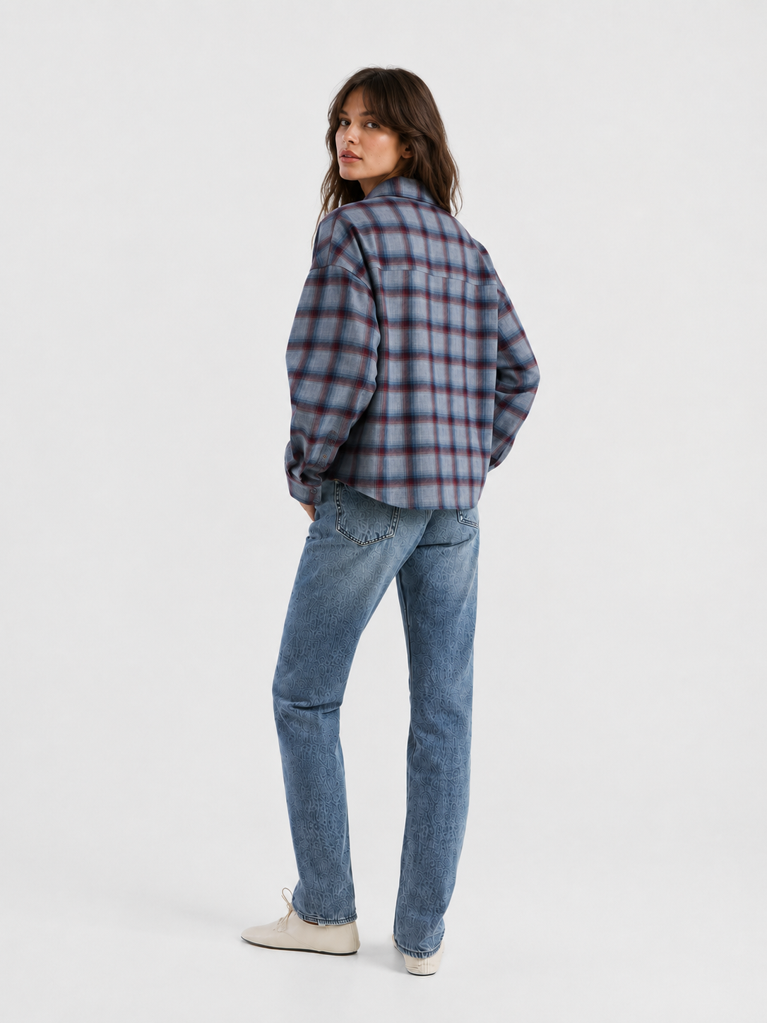 Eine Frau steht mit dem Rücken zur Kamera und blickt über ihre Schulter. Sie trägt das blau-rote Ted-Flanell-Karohemd, dazu blaue Jeans und weiße Schuhe, vor einem schlichten weißen Hintergrund.