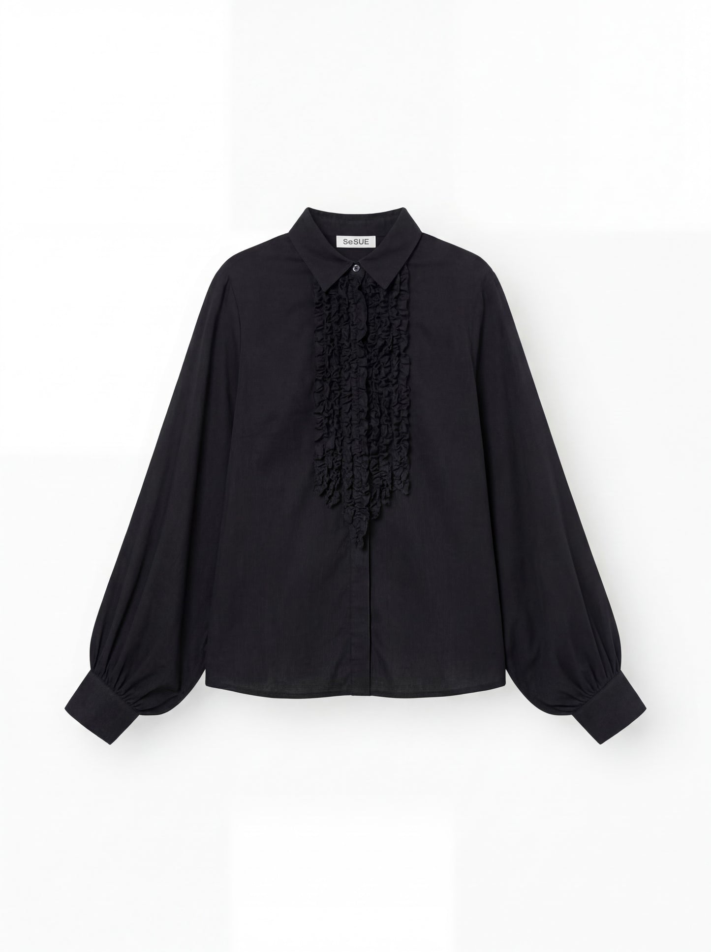 Die Antonia Slim Ruffle Black ist eine schwarze, langärmelige Bluse mit spitzem Kragen, Rüschendetails auf der Vorderseite und breiten Manschetten, die auf einem schlichten weißen Hintergrund gezeigt wird.