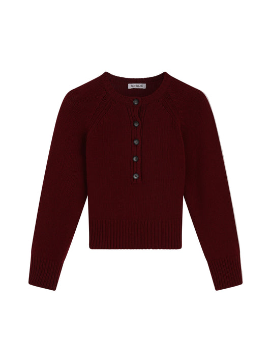 Der Pullover Raglan Burgundy ist ein langärmeliger Damenpullover aus Merinowolle in Dunkelrot. Er hat einen Rundhalsausschnitt, gerippte Bündchen und einen gerippten Saum sowie eine Knopfleiste mit fünf dunklen Knöpfen.