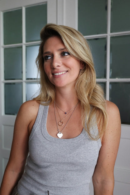 Eine Frau mit langen blonden Haaren trägt das Tank Top Rip Grey und mehrlagige Halsketten, lächelt durch die Glastüren und präsentiert nachhaltige Damenmode.