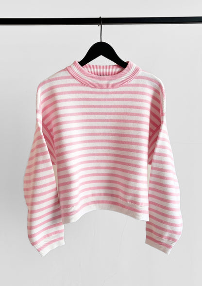 Der Pullover Sailor Rosa White, ein rosa-weißer, horizontal gestreifter, langärmeliger Pullover, hängt auf einem schwarzen Bügel vor einem schlichten weißen Hintergrund.