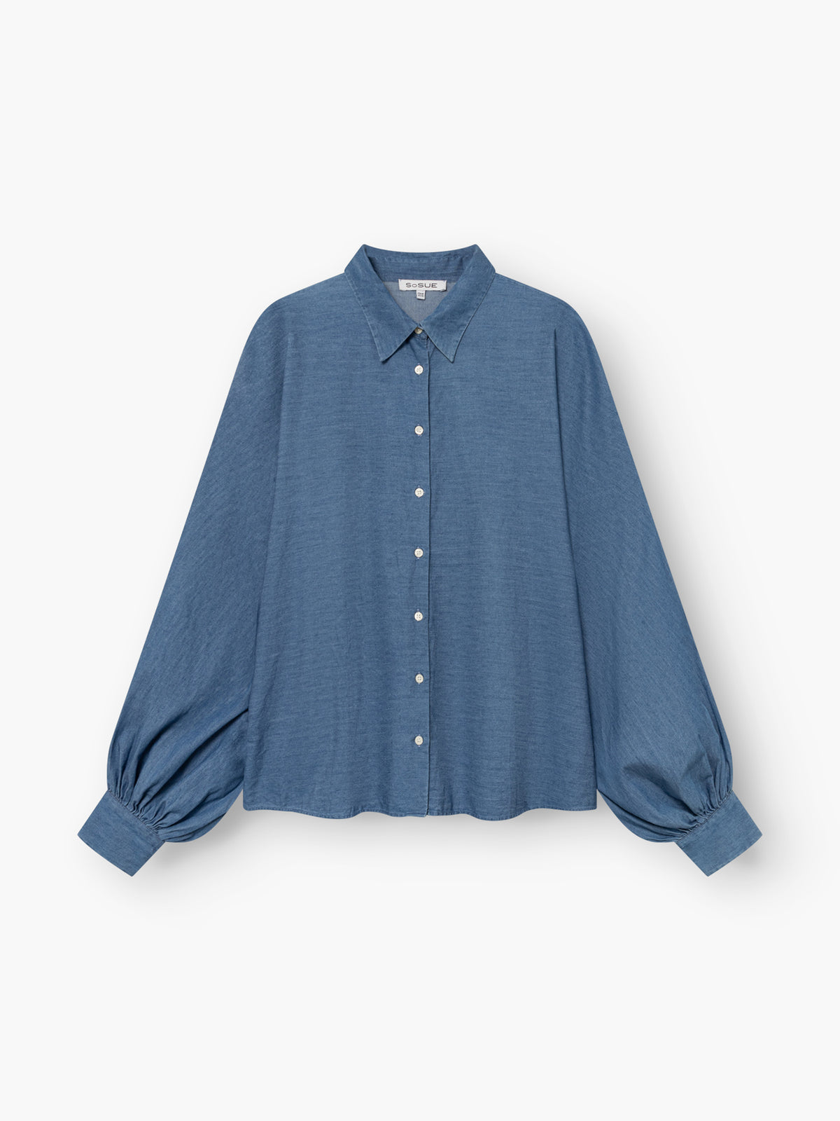 Eine locker sitzende, langärmelige blaue Bluse „Antonia Slim Denim“ mit Kragen und Knopfleiste, deren weite Ärmel an den Manschetten gerafft sind, vor weißem Hintergrund. Diese in Portugal aus hochwertiger Baumwolle gefertigte Bluse vereint einen lässigen Stil mit hochwertiger Verarbeitung.
