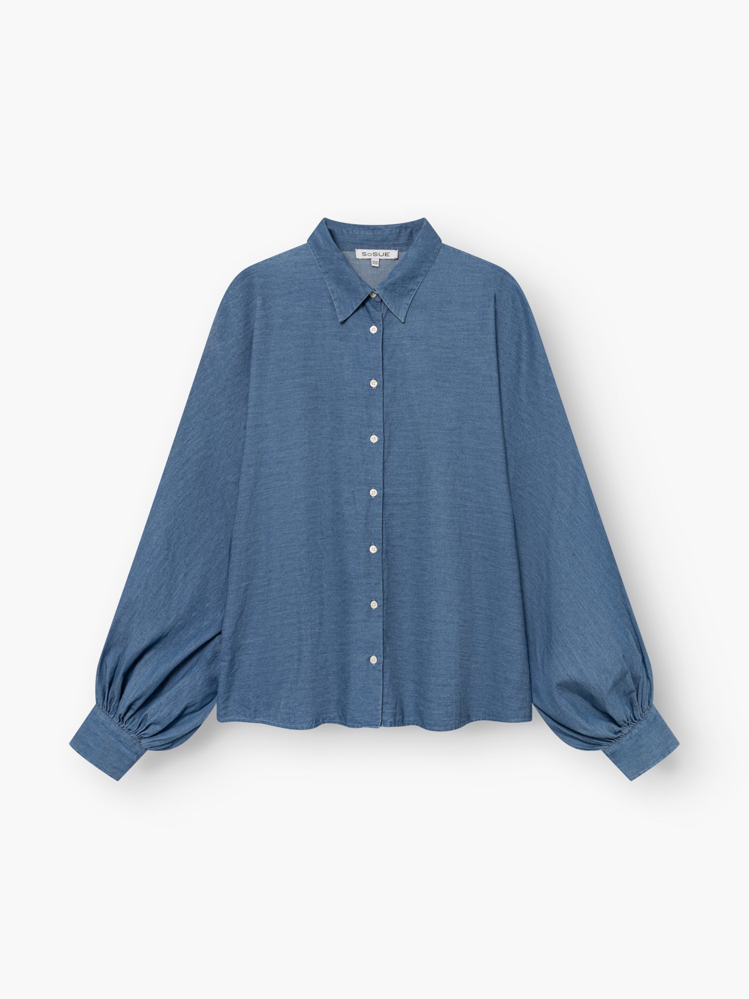 Eine locker sitzende, langärmelige blaue Bluse „Antonia Slim Denim“ mit Kragen und Knopfleiste, deren weite Ärmel an den Manschetten gerafft sind, vor weißem Hintergrund. Diese in Portugal aus hochwertiger Baumwolle gefertigte Bluse vereint einen lässigen Stil mit hochwertiger Verarbeitung.