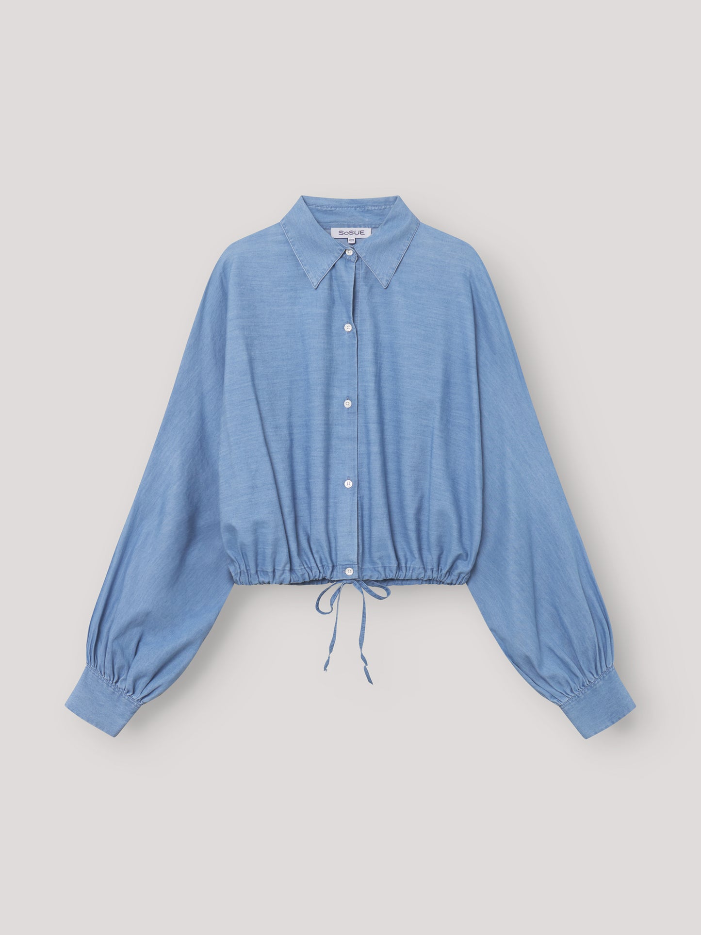 Die Bluse Antonia Drawstring Denim ist eine hellblaue, langärmelige Bluse mit Kragen, elastischen Bündchen und einer lockeren Passform. Der Kordelzug am Saum verleiht dieser stylischen Damenbluse im Denim-Look einen lässigen Touch.