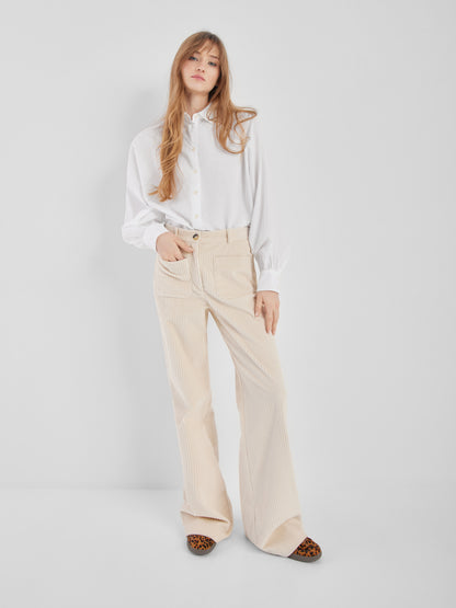 Eine Frau mit langem, gewelltem blondem Haar steht vor einem schlichten weißen Hintergrund und trägt die Bluse Antonia Slim White, eine beigefarbene Hose mit weitem Bein und Schuhe mit Leopardenmuster. Sie hat einen entspannten und selbstbewussten Ausdruck.