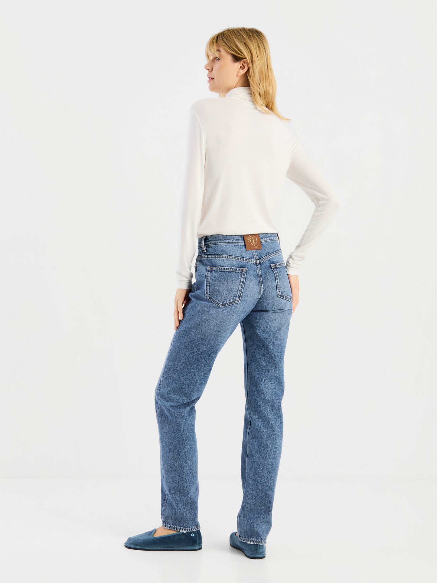 Eine Person steht mit dem Rücken zur Kamera und trägt das langärmelige „Turtle Jersey White“, kombiniert mit einer blauen Straight-Leg-Jeans und blauen Schuhen, vor einem schlichten weißen Hintergrund. Der klassische Look wird durch die erstklassige Qualität des „Turtle Jersey White“ unterstrichen, das stolz in Portugal hergestellt wird.