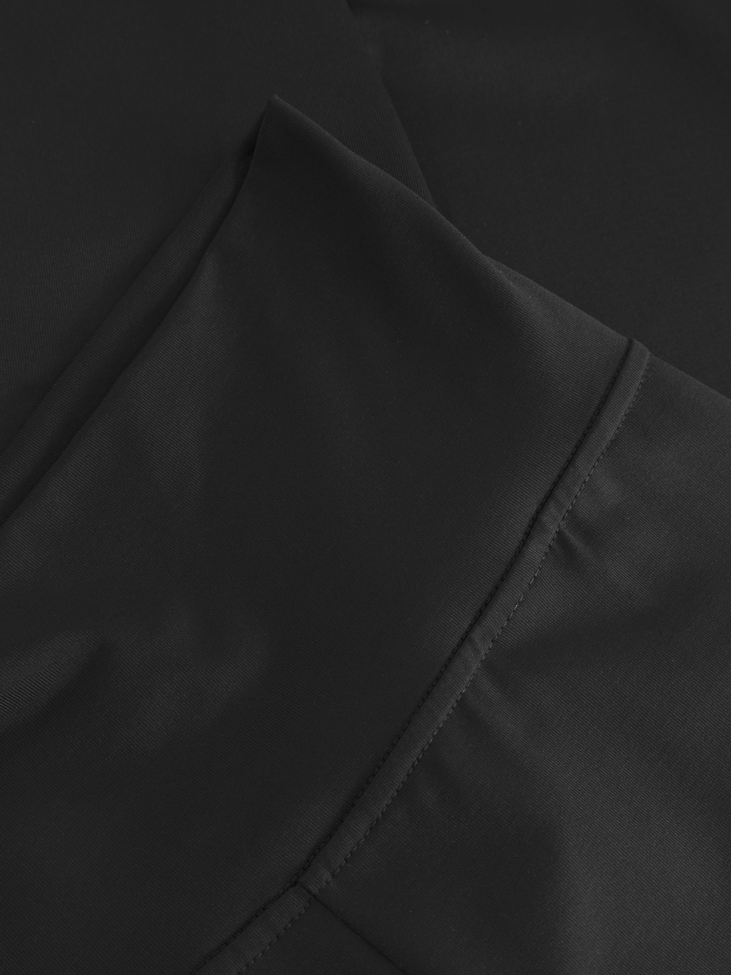 Nahaufnahme von schwarzem Stoff mit sichtbaren Nähten, wahrscheinlich von Leggings Black. Das Material sieht glatt und leicht glänzend aus und ist perfekt für bequeme Damenleggings.