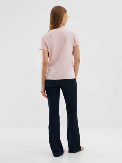 Eine Frau mit glattem, hellbraunem Haar steht vor einem einfarbig weißen Hintergrund. Sie trägt ein T-Shirt Rose aus Baumwolle, dunkelblaue Schlagjeans und eine Sonnenbrille.