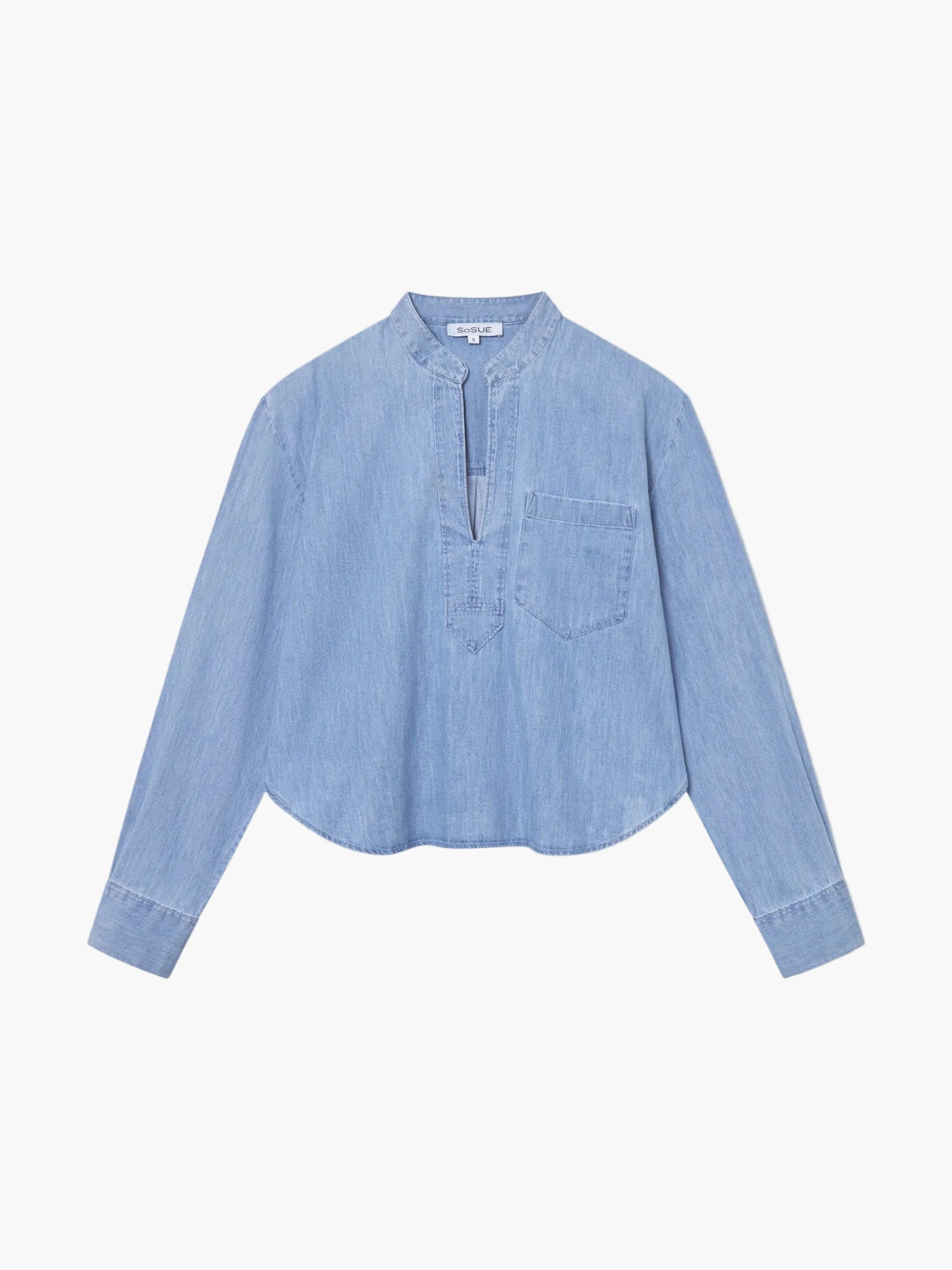 Die Bluse Polo Denim ist eine hellblaue, langärmelige Bluse mit Mandarinenkragen, V-Ausschnitt, Brusttasche und abgerundetem Saum, die flach auf einem einfarbig weißen Hintergrund liegt.