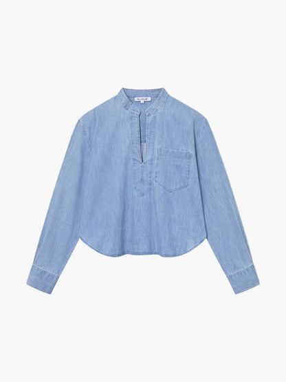 Die Bluse Polo Denim ist eine hellblaue, langärmelige Bluse mit Mandarinenkragen, V-Ausschnitt, Brusttasche und abgerundetem Saum, die flach auf einem einfarbig weißen Hintergrund liegt.