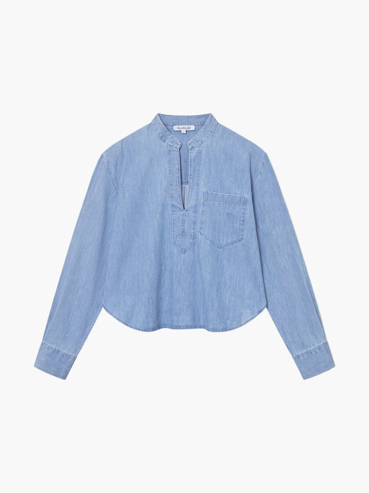 Die Bluse Polo Denim ist eine hellblaue, langärmelige Bluse mit Mandarinenkragen, V-Ausschnitt, Brusttasche und abgerundetem Saum, die flach auf einem einfarbig weißen Hintergrund liegt.