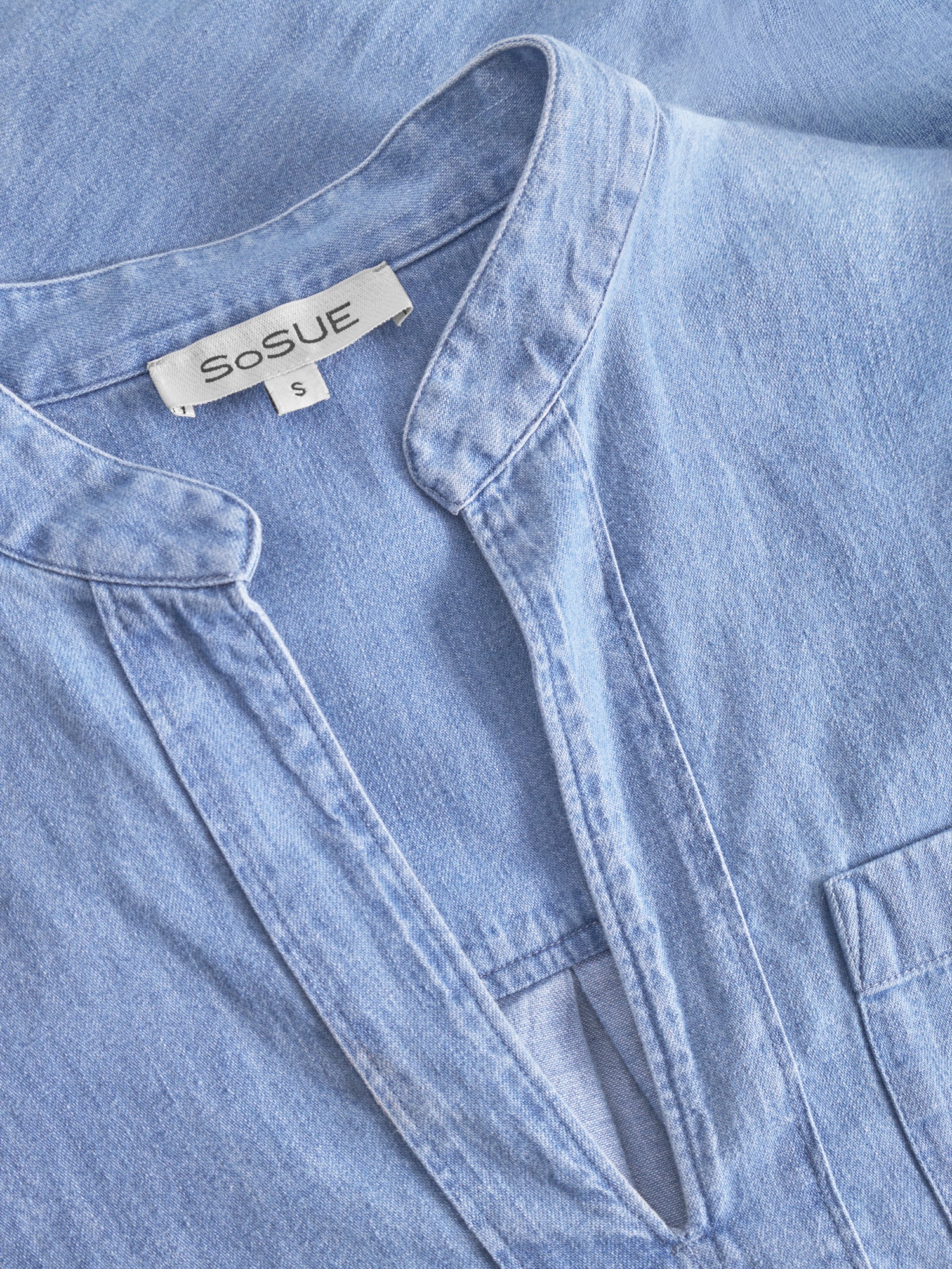 Nahaufnahme des hellblauen Bluse Polo Denim mit Mandarinkragen, V-Ausschnitt, sichtbarem SoSUE-Label am Halsausschnitt und einer partiellen Brusttasche für ein stilvolles Finish.