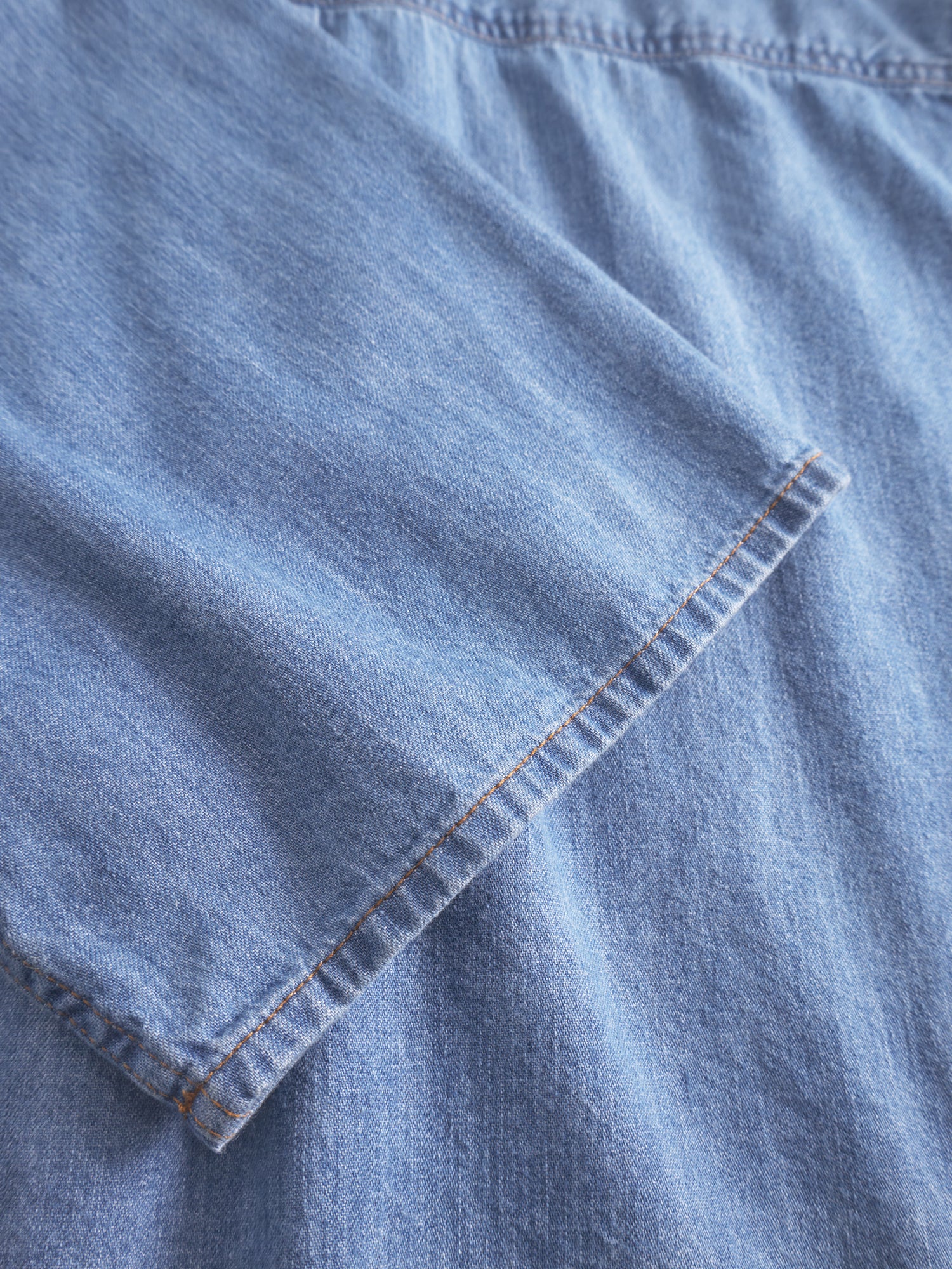 Nahaufnahme der Bluse Short Sleeve Denim in Blau. Hervorzuheben sind die kurzen Ärmel mit sichtbaren Nähten und Nahtdetails. Dieser taillierte Stil betont die klassische Denim-Textur und die fachmännische Verarbeitung.