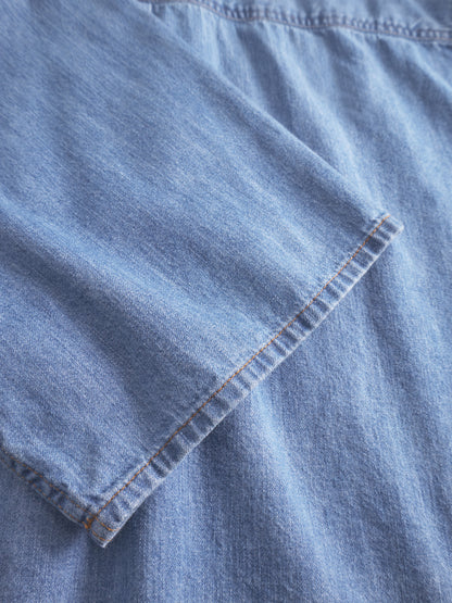 Nahaufnahme der Bluse Short Sleeve Denim in Blau. Hervorzuheben sind die kurzen Ärmel mit sichtbaren Nähten und Nahtdetails. Dieser taillierte Stil betont die klassische Denim-Textur und die fachmännische Verarbeitung.