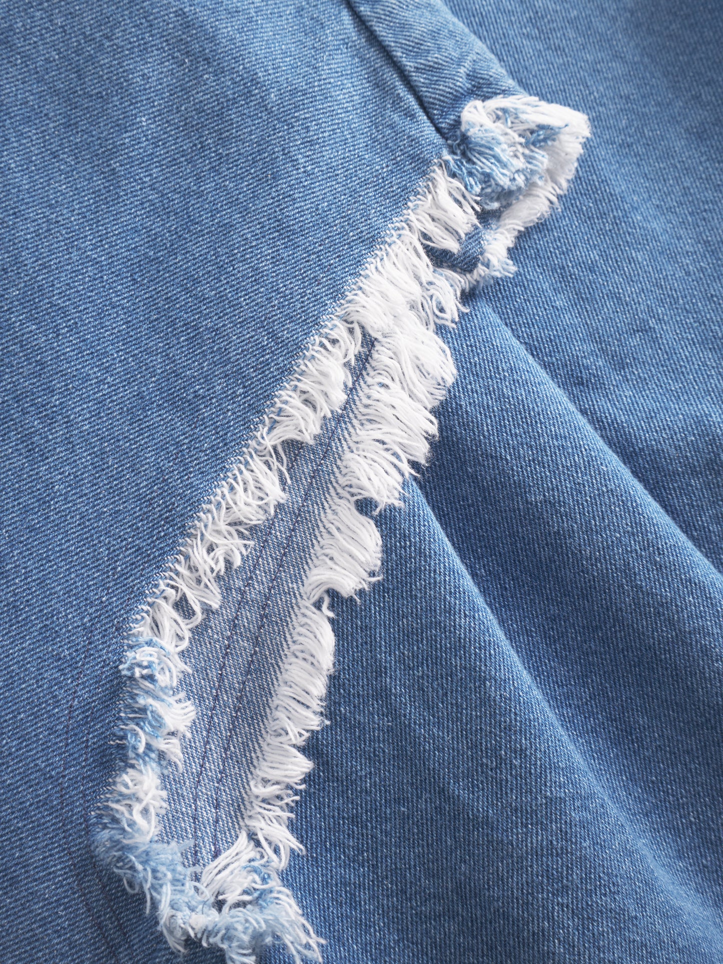 Nahaufnahme eines blauen Denim-Stoffes mit ausgefranster Naht, in der die "Distressed"-Textur zum Vorschein kommt - die perfekte Inspiration für ein trendiges Barcelona Denim Vol 2-Teil oder einen entspannten Sommerlook.