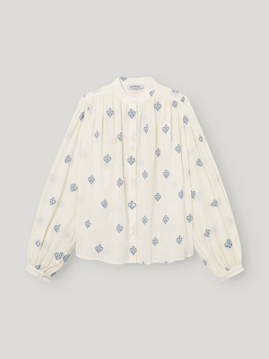 Die Bluse Embroidery ist eine weiße Damenbluse mit langen Ärmeln, einem hohen Kragen, plissierter Vorderseite, blauer geometrischer Blumenstickerei, geknöpften Manschetten und einer entspannten Passform für mühelosen Stil.