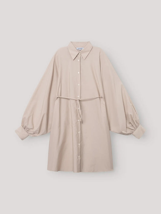 Das Kleid Antonia Dress Vol. 2 Beige ist ein beigefarbenes Hemdkleid mit Kragen und Knopfleiste, langen Puffärmeln, gerafften Manschetten und einem schmalen, passenden Gürtel in der Taille, das vor einem schlichten, hellen Hintergrund gezeigt wird.