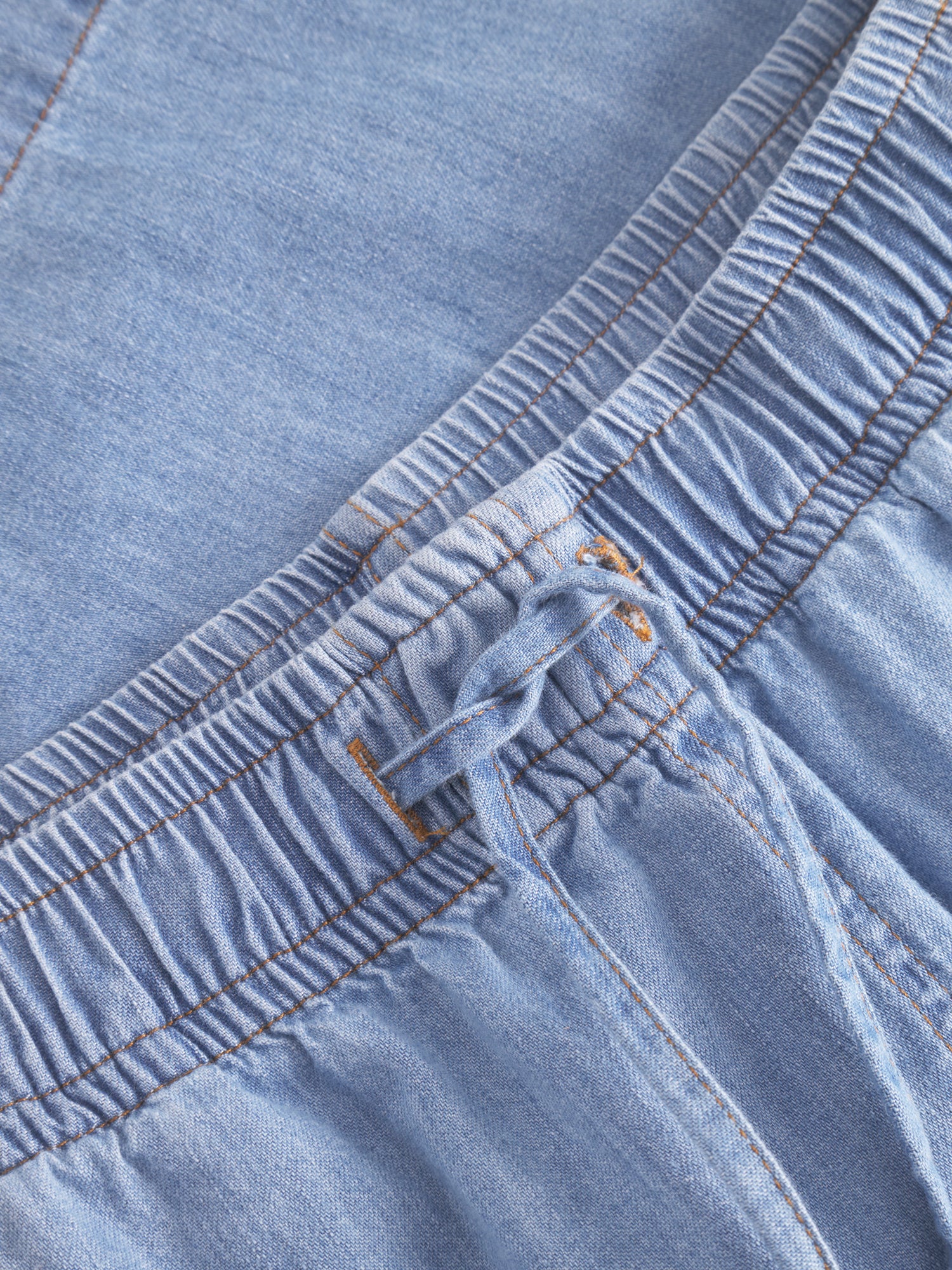 Nahaufnahme der Shorts Light Denim mit elastischem Bund mit Kordelzug, sichtbaren Nähten und gerafftem Stoff.
