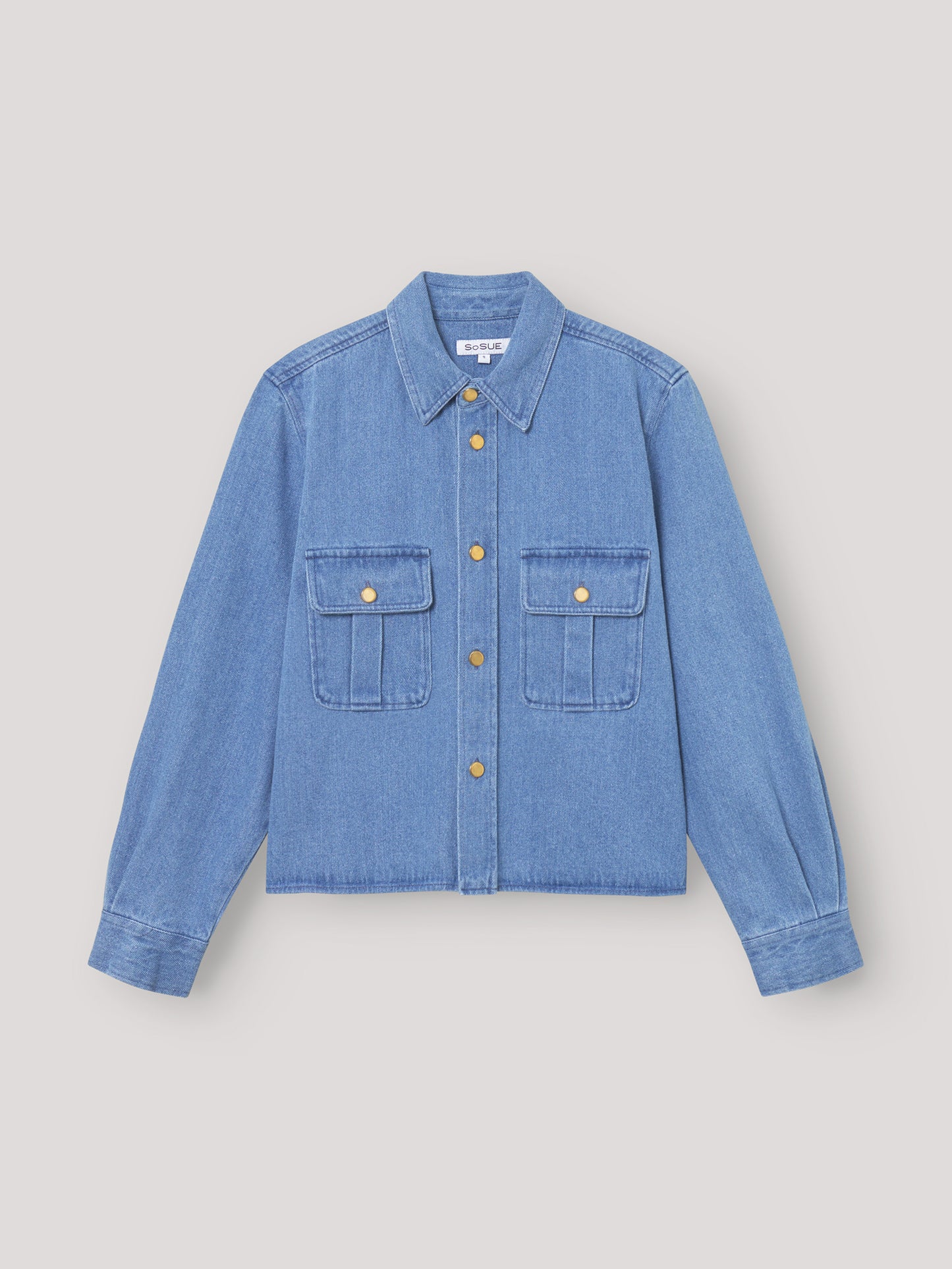 Die Jacke Military ist ein hellblaues Jeanshemd zum Aufknöpfen mit Kragen, langen Ärmeln, zwei Brusttaschen mit goldenen Knöpfen und einer lockeren, kastenförmigen Passform, inspiriert vom SoSUE-Stil und dem klassischen Military Jacket Damen-Design.