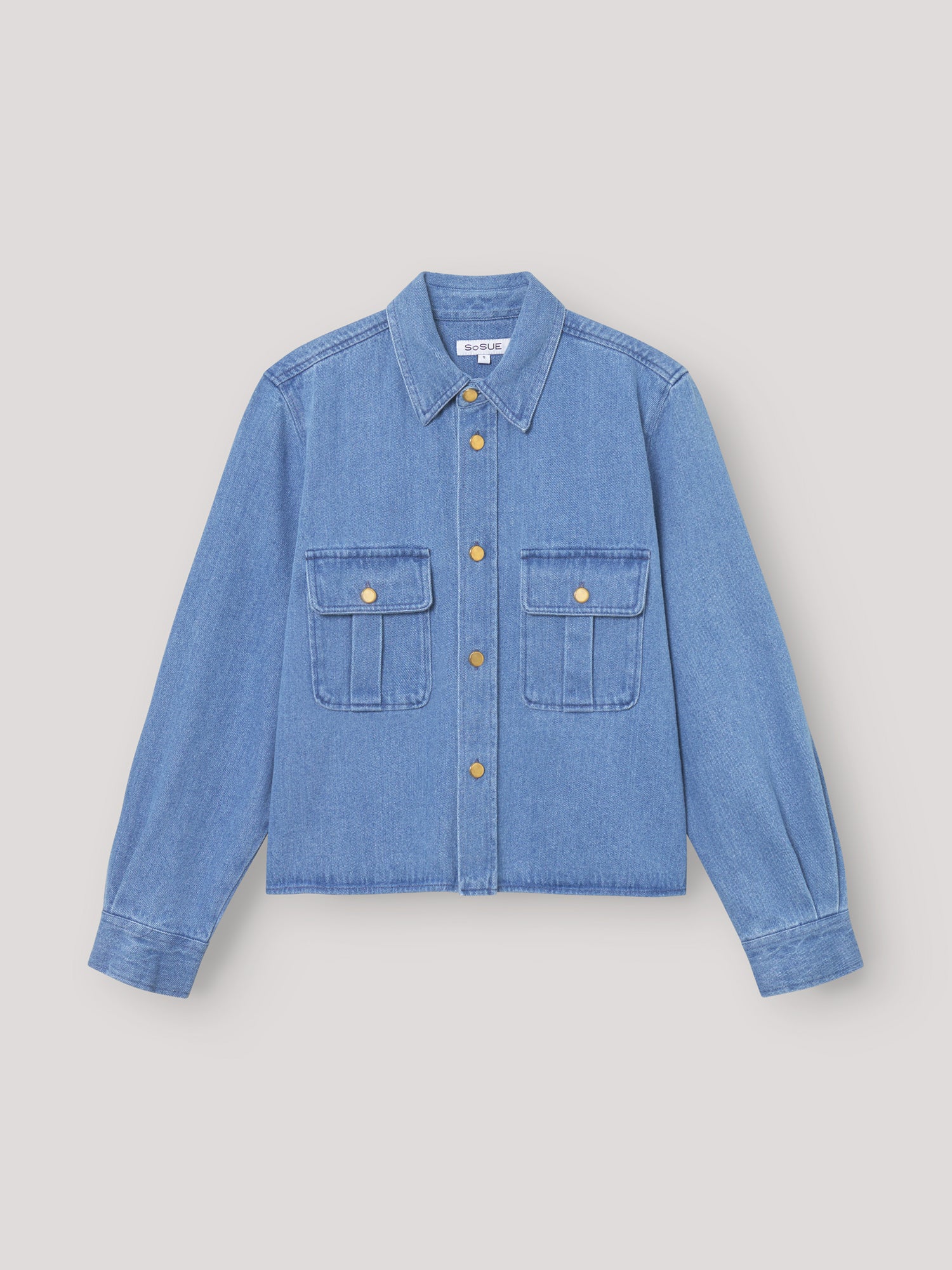 Die Jacke Military ist ein hellblaues Jeanshemd zum Aufknöpfen mit Kragen, langen Ärmeln, zwei Brusttaschen mit goldenen Knöpfen und einer lockeren, kastenförmigen Passform, inspiriert vom SoSUE-Stil und dem klassischen Military Jacket Damen-Design.