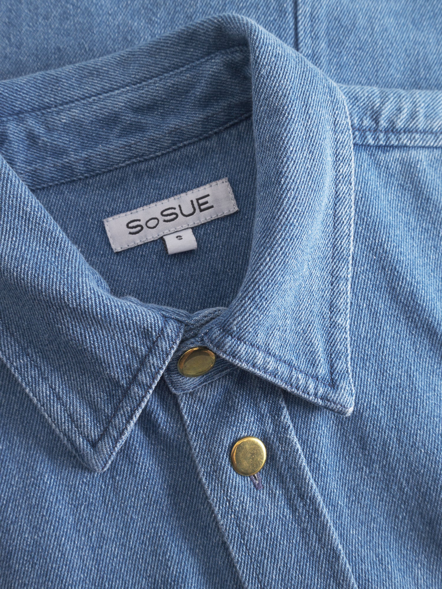 Eine Nahaufnahme eines blauen Hemdes, gepaart mit der stilvollen Jacke Military, zeigt einen modernen und vielseitigen Look.