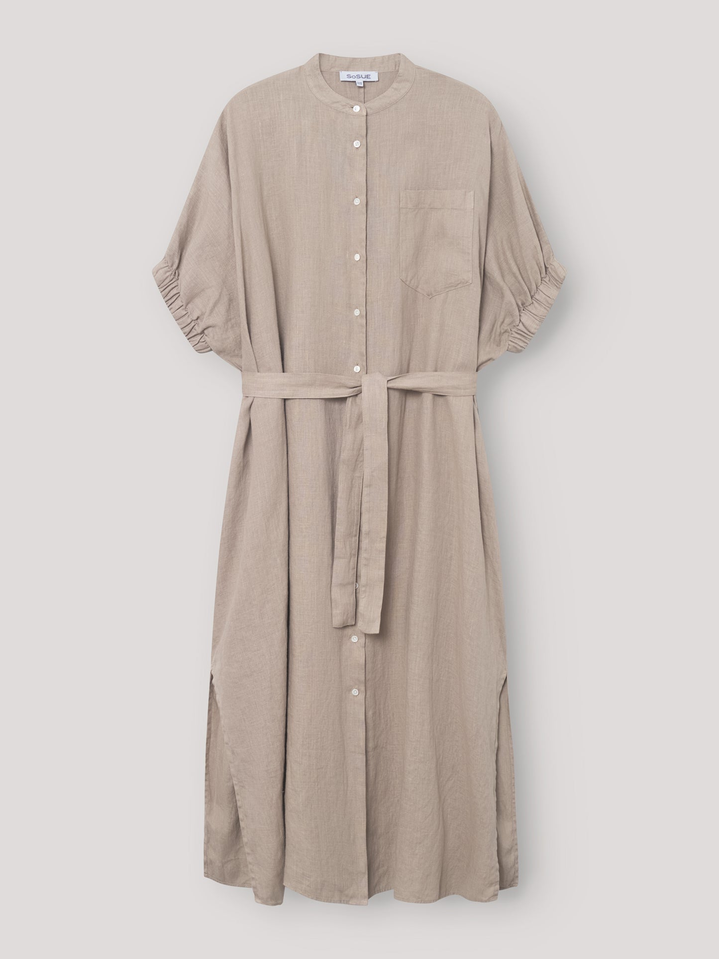 Das Kleid Cowboy Button Linen Mud ist ein hellbeiges Midikleid mit kurzen Ärmeln, einer Brusttasche, einem Stoffgürtel und Seitenschlitzen. Es hängt elegant vor einem schlichten hellen Hintergrund.