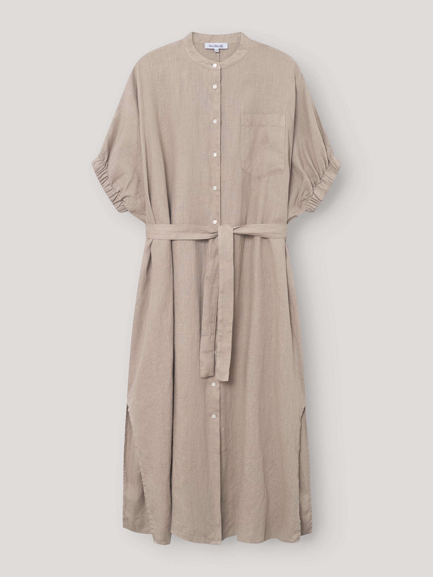 Das Kleid Cowboy Button Linen Mud ist ein hellbeiges Midikleid mit kurzen Ärmeln, einer Brusttasche, einem Stoffgürtel und Seitenschlitzen. Es hängt elegant vor einem schlichten hellen Hintergrund.