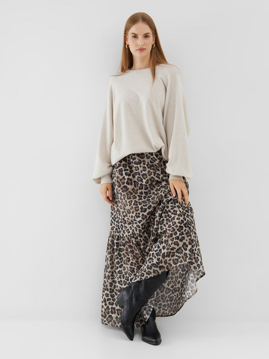 Eine Frau mit glattem, hellbraunem Haar und neutralem Gesichtsausdruck steht vor einem schlichten Hintergrund und trägt den Pullover Elli Beige, einen langen Stufenrock mit Leopardenmuster und schwarze Stiefel.