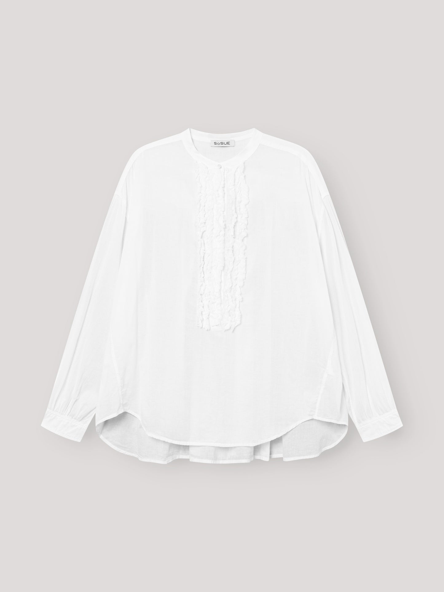 Die Bluse Bruna white ist eine langärmelige, locker sitzende Damenbluse mit Rundhalsausschnitt und eleganten Rüschendetails auf der Vorderseite, die auf einem hellgrauen Hintergrund zu sehen ist.