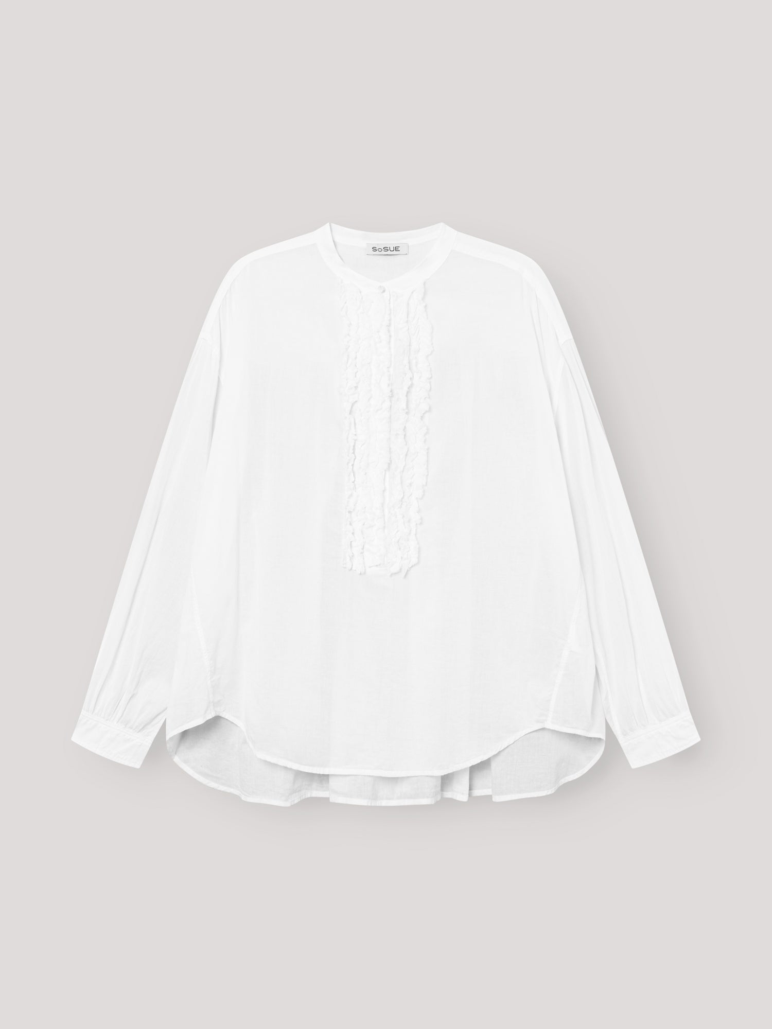 Die Bluse Bruna white ist eine langärmelige, locker sitzende Damenbluse mit Rundhalsausschnitt und eleganten Rüschendetails auf der Vorderseite, die auf einem hellgrauen Hintergrund zu sehen ist.