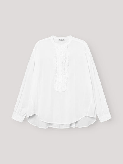 Die Bluse Bruna white ist eine langärmelige, locker sitzende Damenbluse mit Rundhalsausschnitt und eleganten Rüschendetails auf der Vorderseite, die auf einem hellgrauen Hintergrund zu sehen ist.