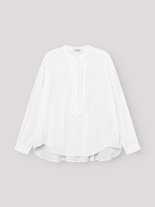 Die Bluse Bruna white ist eine langärmelige, locker sitzende Damenbluse mit Rundhalsausschnitt und eleganten Rüschendetails auf der Vorderseite, die auf einem hellgrauen Hintergrund zu sehen ist.