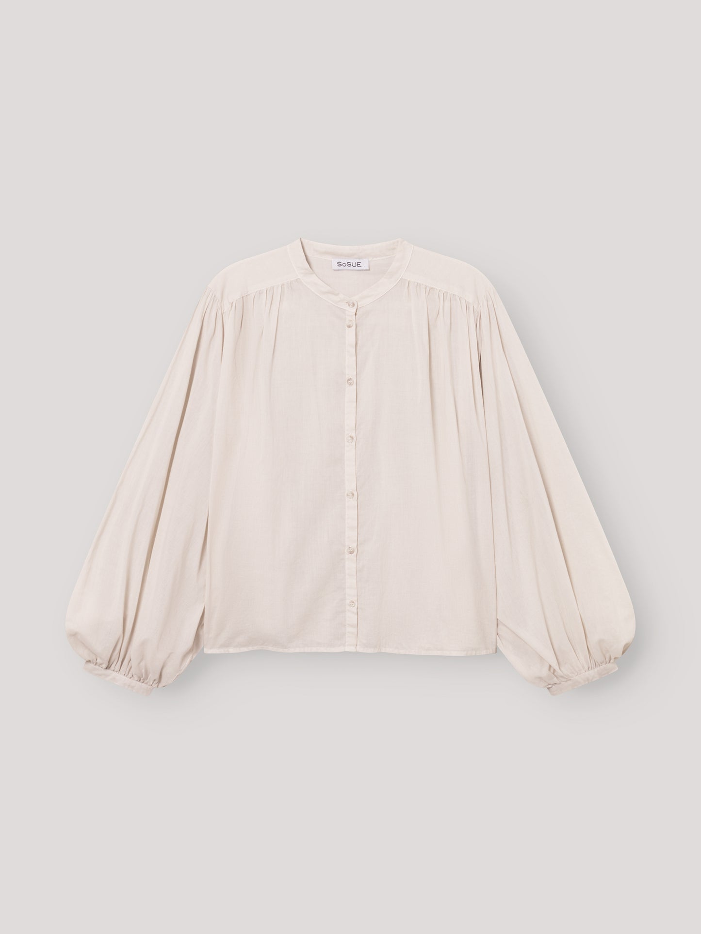 Die Bluse Bella Beige ist eine lockere, übergroße cremefarbene Bluse mit langen, weiten Ärmeln, Rundhalsausschnitt, Knopfleiste, gerafften Schultern und elastischen Bündchen - ideal als elegante Damenbluse Beige für stilvollen Komfort.