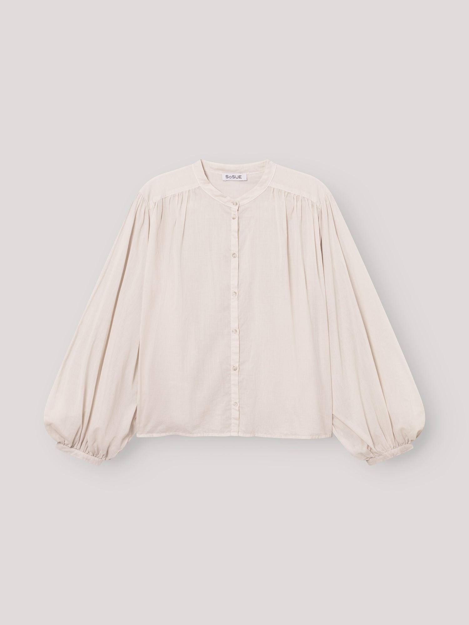 Die Bluse Bella Beige ist eine lockere, übergroße cremefarbene Bluse mit langen, weiten Ärmeln, Rundhalsausschnitt, Knopfleiste, gerafften Schultern und elastischen Bündchen - ideal als elegante Damenbluse Beige für stilvollen Komfort.