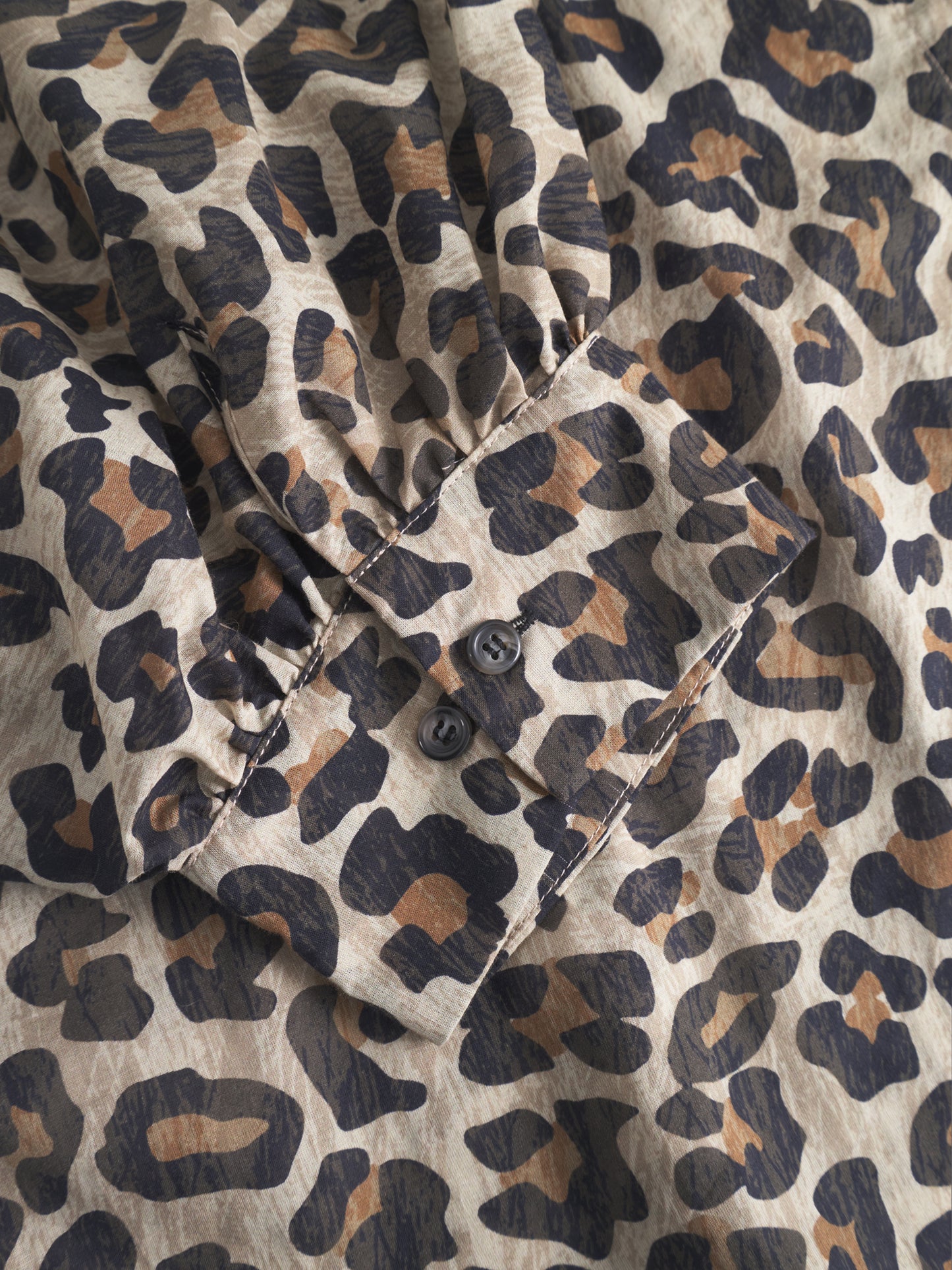Eine Nahaufnahme des Bluse Antonia Short Sleeve Leo zeigt den beigen, braunen und schwarzen Leopardenprint und eine geknöpfte Manschette mit zwei dunklen Knöpfen.