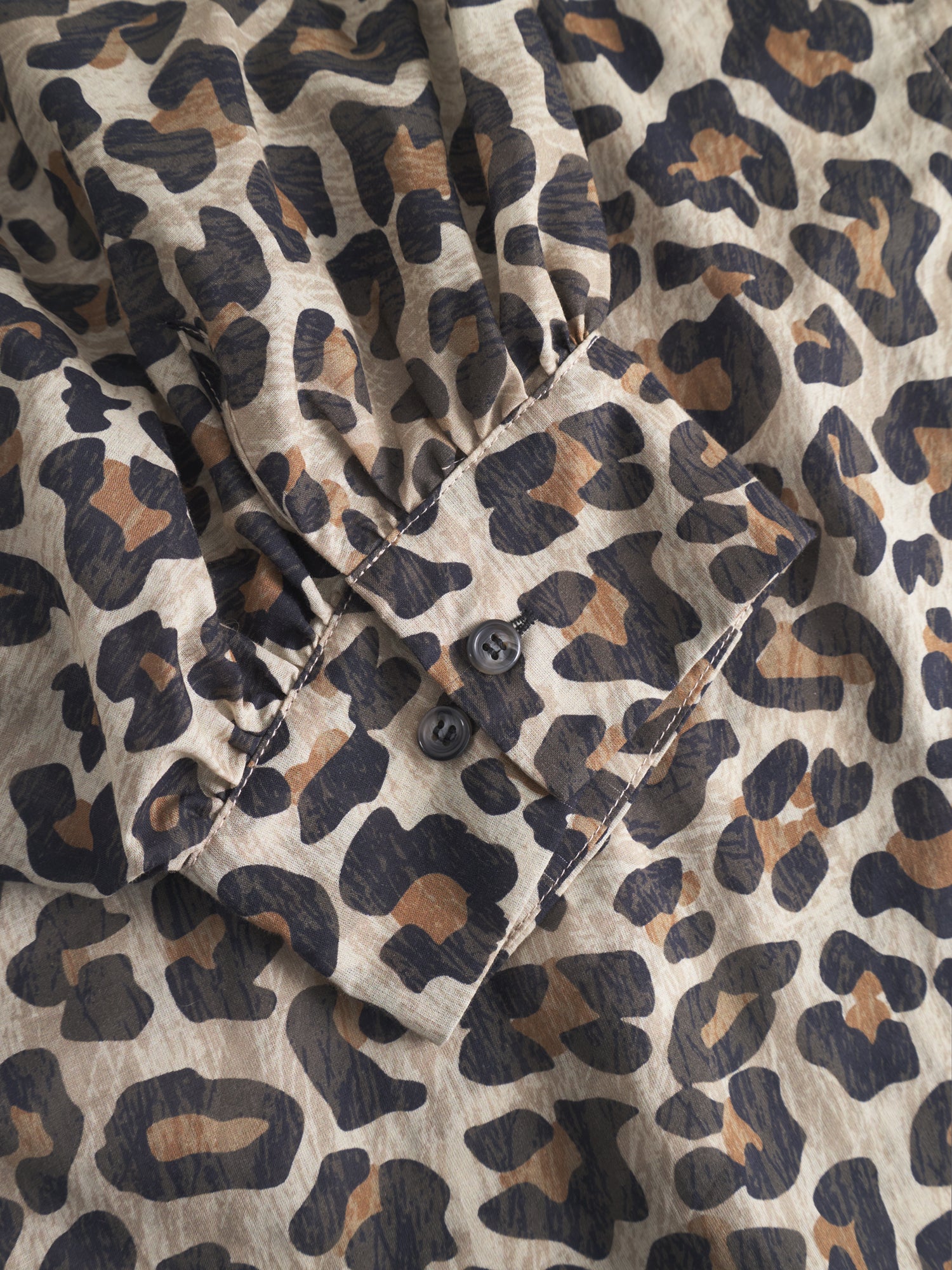 Eine Nahaufnahme des Bluse Antonia Short Sleeve Leo zeigt den beigen, braunen und schwarzen Leopardenprint und eine geknöpfte Manschette mit zwei dunklen Knöpfen.
