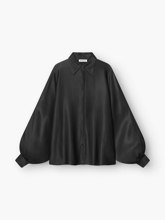 Die Bluse Antonia Shiny Black ist eine locker sitzende Satinbluse mit Kragen, Knopfleiste und weiten, langen Ärmeln, die an den Manschetten gerafft sind, um einen eleganten Oversized-Look zu erzielen, abgebildet auf weißem Grund.