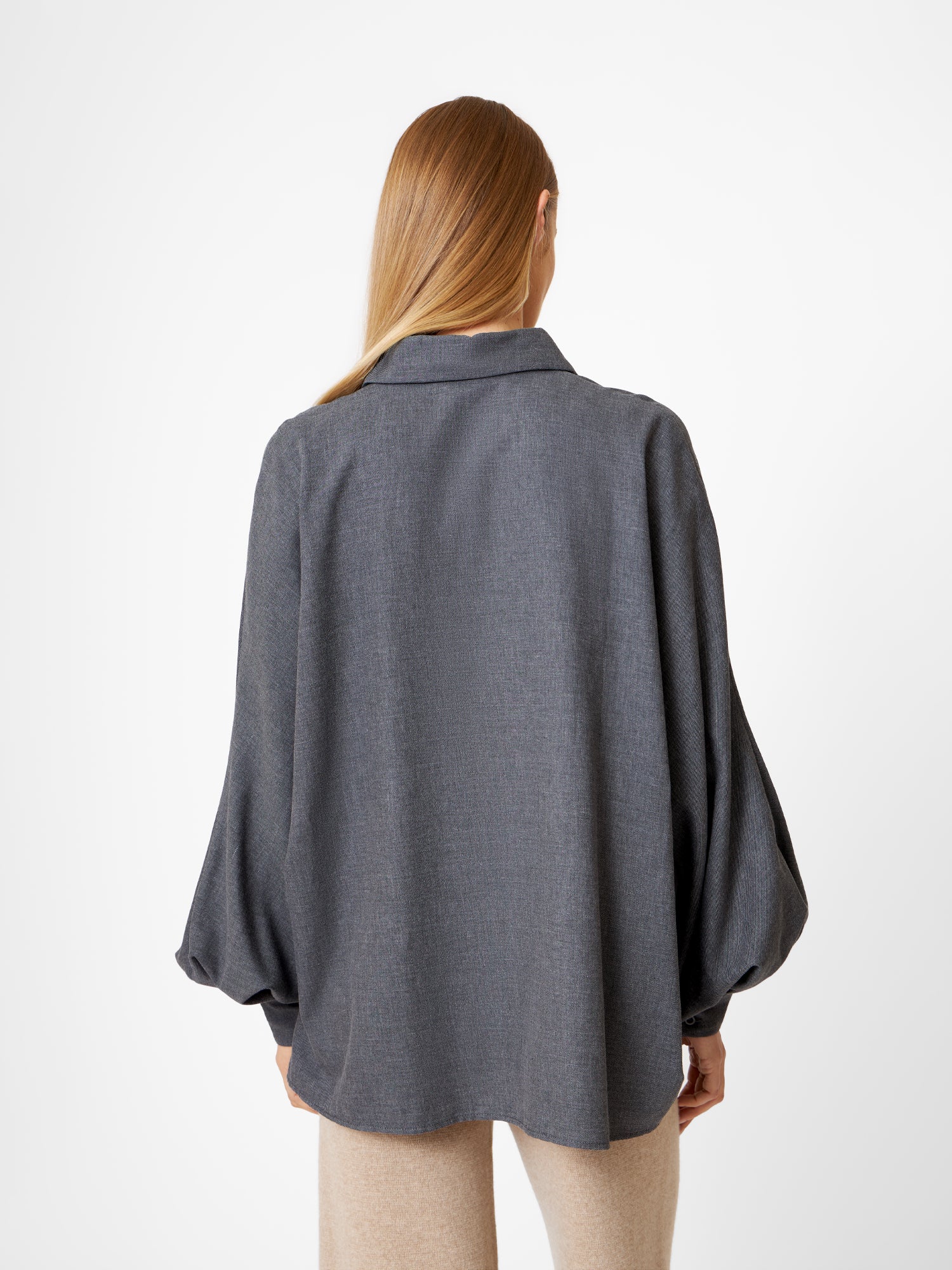 Eine Person mit langem, glattem Haar wird von hinten gezeigt. Sie trägt die Bluse Antonia Flanell Anthra mit weiten Ärmeln und beiger Hose vor einem schlichten weißen Hintergrund.