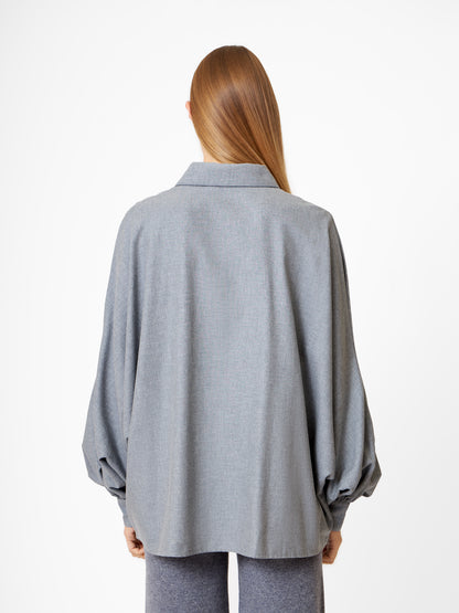 Eine Person mit langem, glattem Haar wird von hinten gezeigt. Sie trägt die Bluse Antonia Grey Flanell mit Ballonärmeln und passender grauer Hose und steht vor einem schlichten weißen Hintergrund.