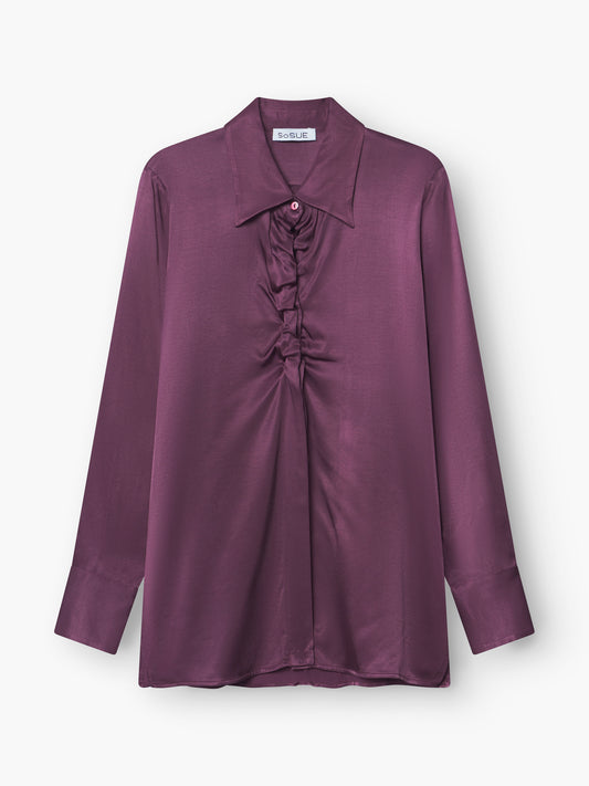 Die Bluse Ella Shiny Purple ist eine langärmelige Satinbluse mit breitem Kragen und gerafften Rüschen in der vorderen Mitte, die auf weißem Hintergrund zu sehen ist.