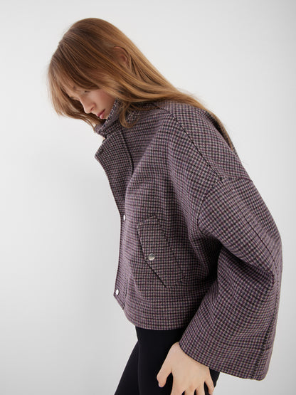 Eine Person mit langem, hellbraunem Haar trägt die Jacke Victoria mit Hahnentrittmuster - locker sitzend mit weiten Ärmeln und Vordertaschen - gepaart mit einer schwarzen Hose für einen stilvollen Übergangsjacke Damen-Look vor einem schlichten hellen Hintergrund.