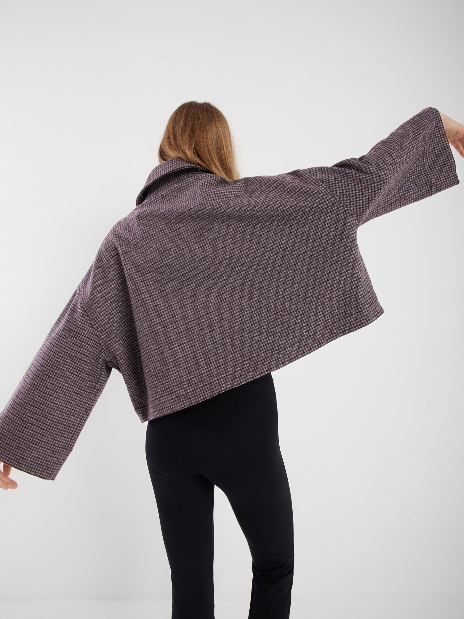 Eine Person mit langem hellbraunem Haar, die den Blick abwendet, trägt die Jacke Victoria mit Hahnentrittmuster und weiten Ärmeln sowie eine schwarze Hose vor einem einfarbig weißen Hintergrund.