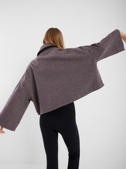 Eine Person mit langem hellbraunem Haar, die den Blick abwendet, trägt die Jacke Victoria mit Hahnentrittmuster und weiten Ärmeln sowie eine schwarze Hose vor einem einfarbig weißen Hintergrund.