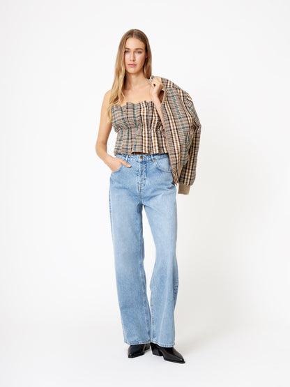 Eine Frau steht vor einem weißen Hintergrund in hellblauen Jeans mit weitem Bein, schwarzen spitzen Schuhen und dem Pleat Top Check schulterfrei Crop Top Damen und trägt eine passende karierte Jacke über einer Schulter. Sie hat lange Haare.