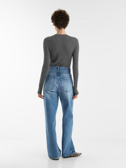 Person, die mit dem Rücken zur Kamera steht und einen grauen, taillierten Kaschmir-Langarm-Anthrazit, Bluejeans mit hoher Taille und flache Schuhe vor einem weißen Hintergrund trägt.