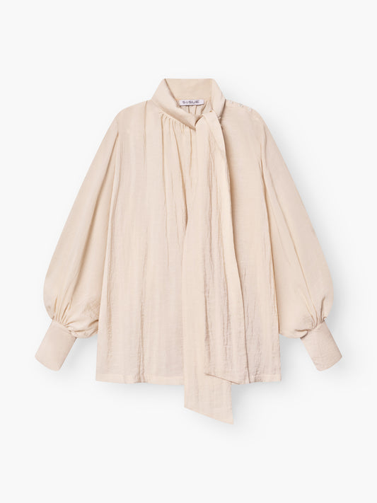 Die Bluse Bombay beige begeistert mit Schleifenkragen, langen Ballonärmeln und lockerer Passform. Ein langer, drapierter Schal am hohen Ausschnitt setzt die leicht strukturierte Qualität elegant in Szene.