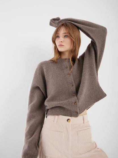 Eine Frau mit hellbraunem Haar posiert mit erhobenem Arm. Sie trägt die locker sitzende, kurz geschnittene Jacke Cashmere Azteco und eine cremefarbene Cordhose mit hoher Taille vor einem schlichten weißen Hintergrund.