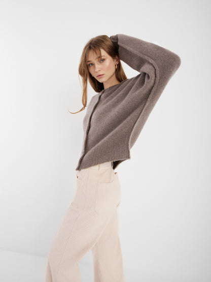 Eine Frau in einer cremefarbenen Jacke Cashmere Azteco und einer cremefarbenen Hose posiert mit einem erhobenen Arm vor einem schlichten weißen Hintergrund.